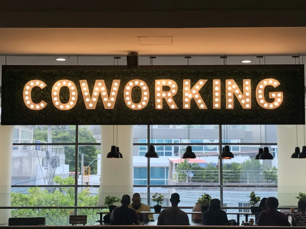 Illuminated coworking sign above people sharing a workspace.